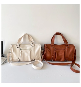 Detailed view of cream and brown Boston bags with rivet tassels and adjustable straps