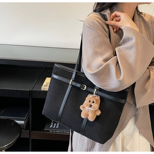 Detail of black suede tote bag with leather straps and cute brown bear pendant charm
