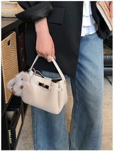 Detail of creamy white litchi leather handbag with gold lock and plush rabbit charm