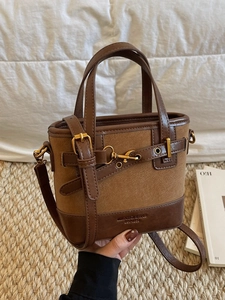 Vintage brown leather bucket bag with top handle and gold buckle on woven background