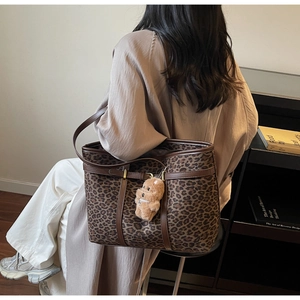 Detailed view of leopard print canvas tote bag with brown leather trim and bear pendant