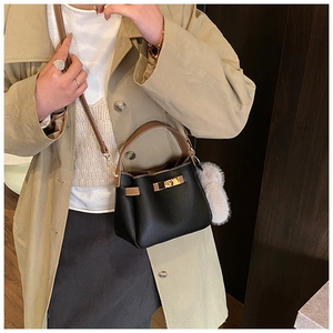 Close-up of black litchi grain bucket bag with brown handle and plush ball charm