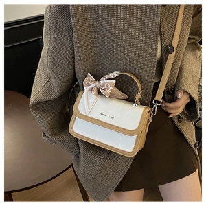 Close-up of stylish white square bag with caramel trim and decorative handle scarf