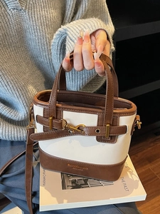 Vintage cream and brown bucket bag with gold buckle hardware on an aesthetic book background