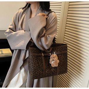Detailed close-up of leopard print tote bag with brown leather handles and plush dog charm