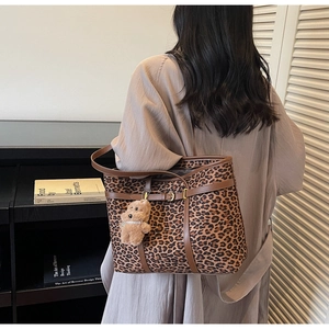 Detail of leopard print tote bag with brown leather straps and plush bear charm