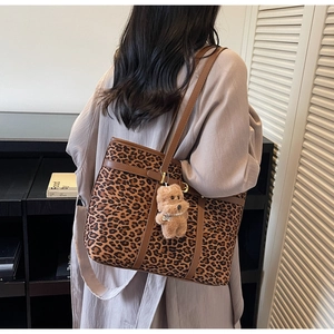 Detail of leopard print tote bag with brown leather handles and teddy bear charm accessory