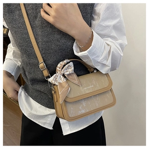 Detail of a beige textured crossbody bag featuring a silk scarf wrap and metal buckles