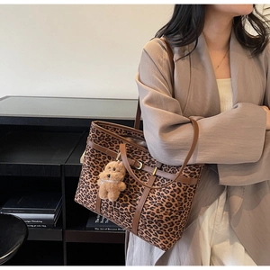 Detail of leopard print tote bag with brown leather handles and teddy bear charm
