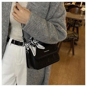 Close-up of a black matte leather square bag with a black and white patterned silk scarf