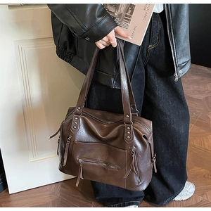 Detail of a large brown vintage tote bag featuring decorative rivets and exterior pockets