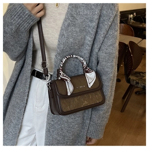 Detail of dark brown leather crossbody bag with decorative silk scarf and fashion text