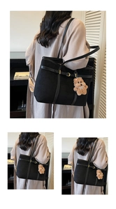 Detail of black suede tote bag with golden buckle and cute plush bear charm accessory