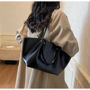 Grand cabas minimaliste en cuir mat noir porté à l'épaule sur un trench-coat classique