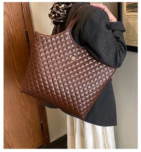 Detailed view of brown quilted tote bag with golden clover logo and chic leather texture