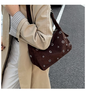 Détail du sac à bandoulière en daim marron foncé avec œillets argentés et zip