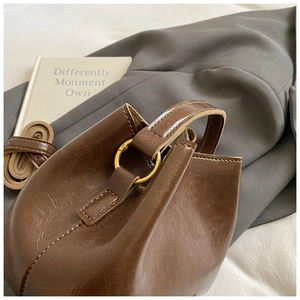Detail der braunen Eimertasche mit geölter Lederstruktur und goldenen Beschlägen