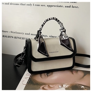 Detail of small crossbody bag featuring contrast piping and silk scarf handle decoration