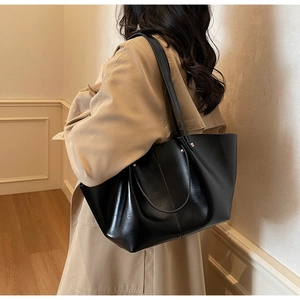 Grand sac cabas noir tendance porté à l'épaule sur un trench-coat kaki pour un look chic