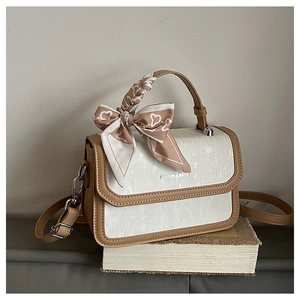Detail of two-tone beige and brown square bag with floral silk scarf on a book