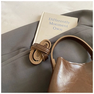 Detail einer dunkelbraunen, glänzenden Eimer-Tasche aus Leder mit verstellbarem Riemen