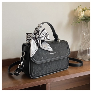 Detail of a black textured crossbody bag with a heart-patterned silk scarf handle