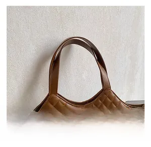Detail of comfortable dual handles and metal clover ornament on brown quilted handbag