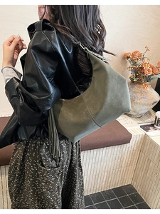 Detail of olive green hobo bag with fringe tassel worn by a model in warm indoor setting