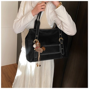 Détail d'un sac cabas noir avec coutures contrastées et pendentif cheval en peluche