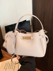 Retro beige bucket bag with litchi texture and plush pompom charm on a wooden table