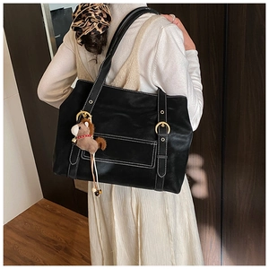 Détail d'un sac cabas en cuir noir avec coutures blanches et breloque cheval pour femme