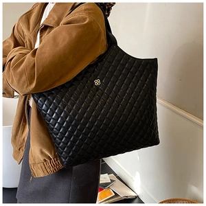 Detail view of a large black quilted tote bag with a golden four-leaf clover logo