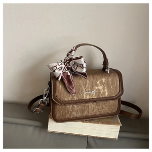 Detail of vintage brown textured crossbody bag with decorative silk scarf and metal logo