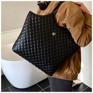 Detail of black quilted tote bag with diamond stitching and golden flower metal logo