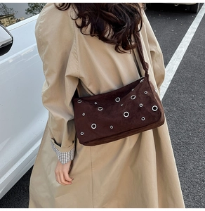 Détail du sac en daim marron avec œillets métalliques porté avec un trench-coat
