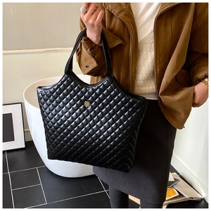Close-up of black quilted tote bag with golden clover logo and elegant matte leather texture