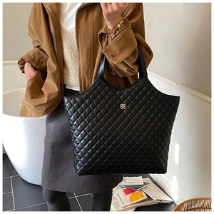 Detail of black quilted tote bag featuring golden floral logo and leather handles