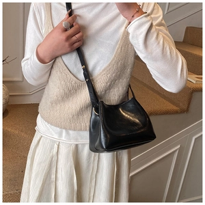 Detailansicht der schwarzen glänzenden Eimertasche mit goldenen Nieten und Schultergurt