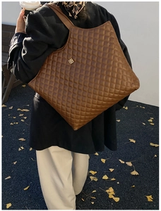 Close-up of brown quilted tote bag with golden floral logo and leather strap detail