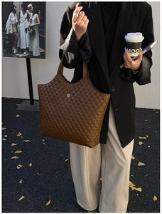 Close-up of brown quilted leather tote bag with gold clover emblem on a street scene