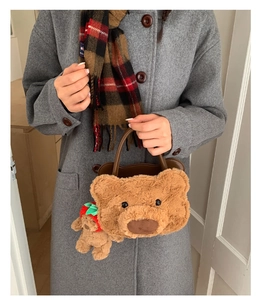Detail of a plush brown bear handbag featuring a strawberry bear charm and leather handles