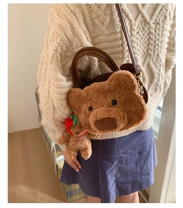 Detail of plush brown bear crossbody bag featuring strawberry charm and leather strap