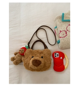 Detail of plush bear crossbody bag featuring soft brown texture and strawberry charm