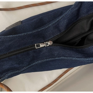 Detailed close-up of dark denim fabric with premium metal zipper and braided strap