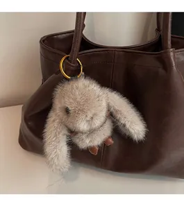 Détail d'un pendentif lapin en peluche avec anneau doré sur un grand sac en cuir