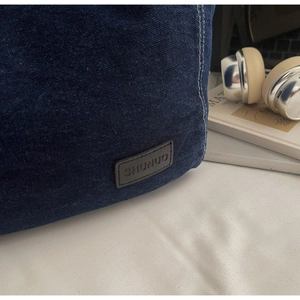 Detail shot of blue denim tote bag featuring a leather SHUNUO logo and quality stitching