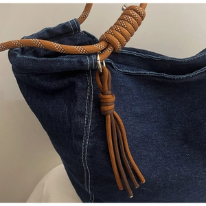 Detail of dark blue denim tote featuring brown braided rope handle and fringe tassel