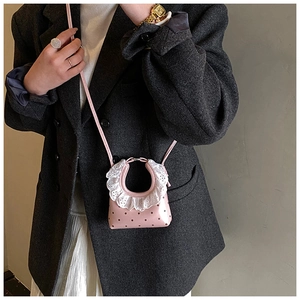 Detail of pink polka dot crossbody bag with white lace trim and slim leather shoulder strap