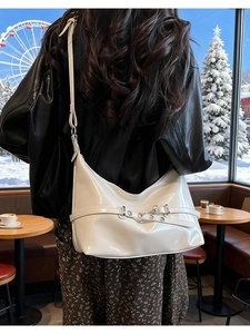 Détail d'un sac à bandoulière en cuir verni blanc avec boucles porté par un mannequin