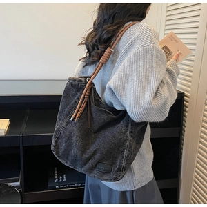 Detail of dark grey denim tote bag featuring brown braided rope shoulder straps and a leather tag